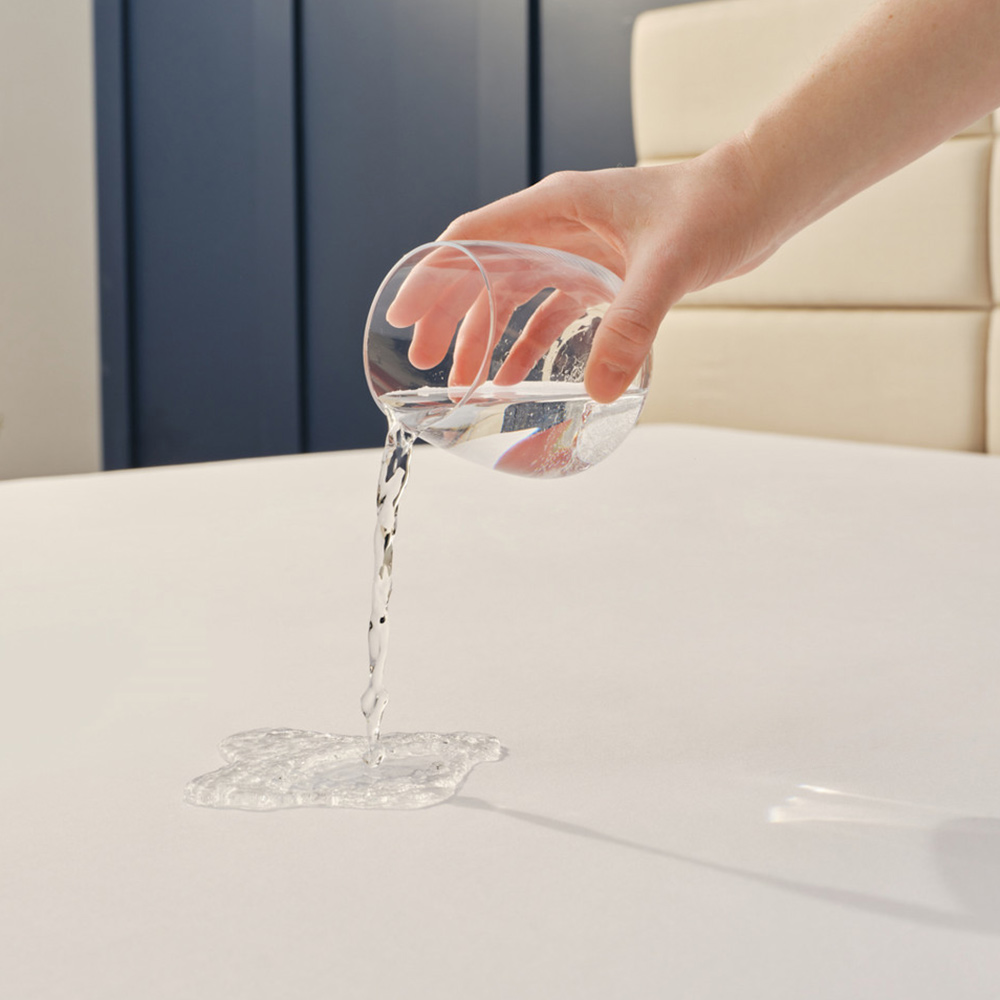 Hand pouring water onto waterproof mattress protector surface