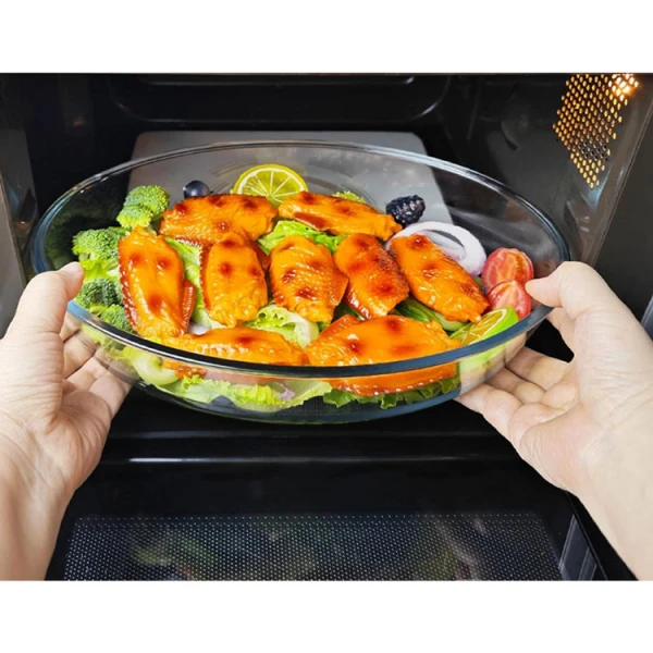 Hands placing oval glass bakeware with food into an oven.