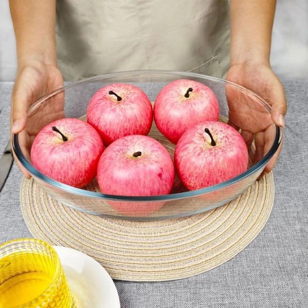 Hands holding an oval glass bakeware with apples.