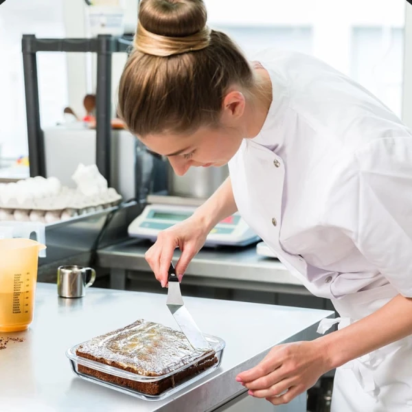 Chef icing a cake in a glass pan.