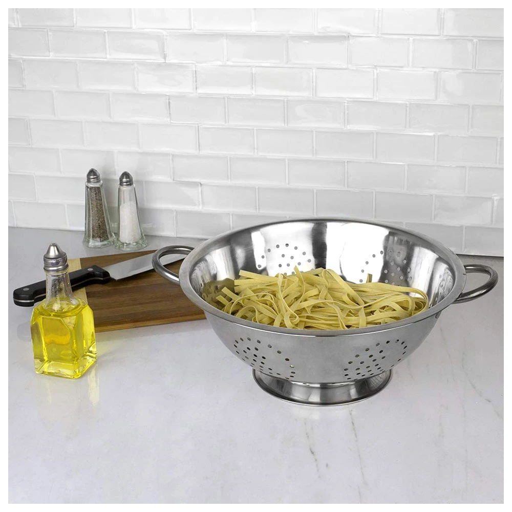 Stainless steel colander filled with pasta on a white kitchen countertop