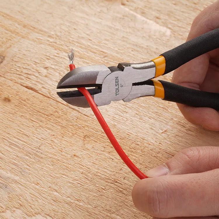 Diagonal cutting pliers cutting red wire on wood surface.